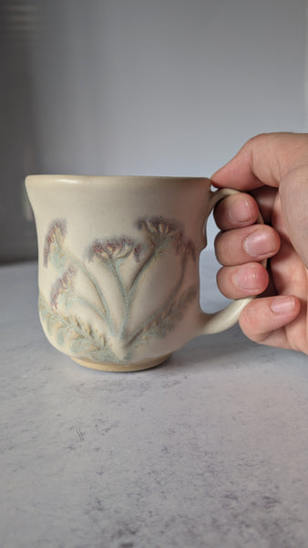 Hand holding a ceramic mug with floral design on a gray surface