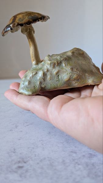 Hand holding a mushroom-shaped object against a neutral background